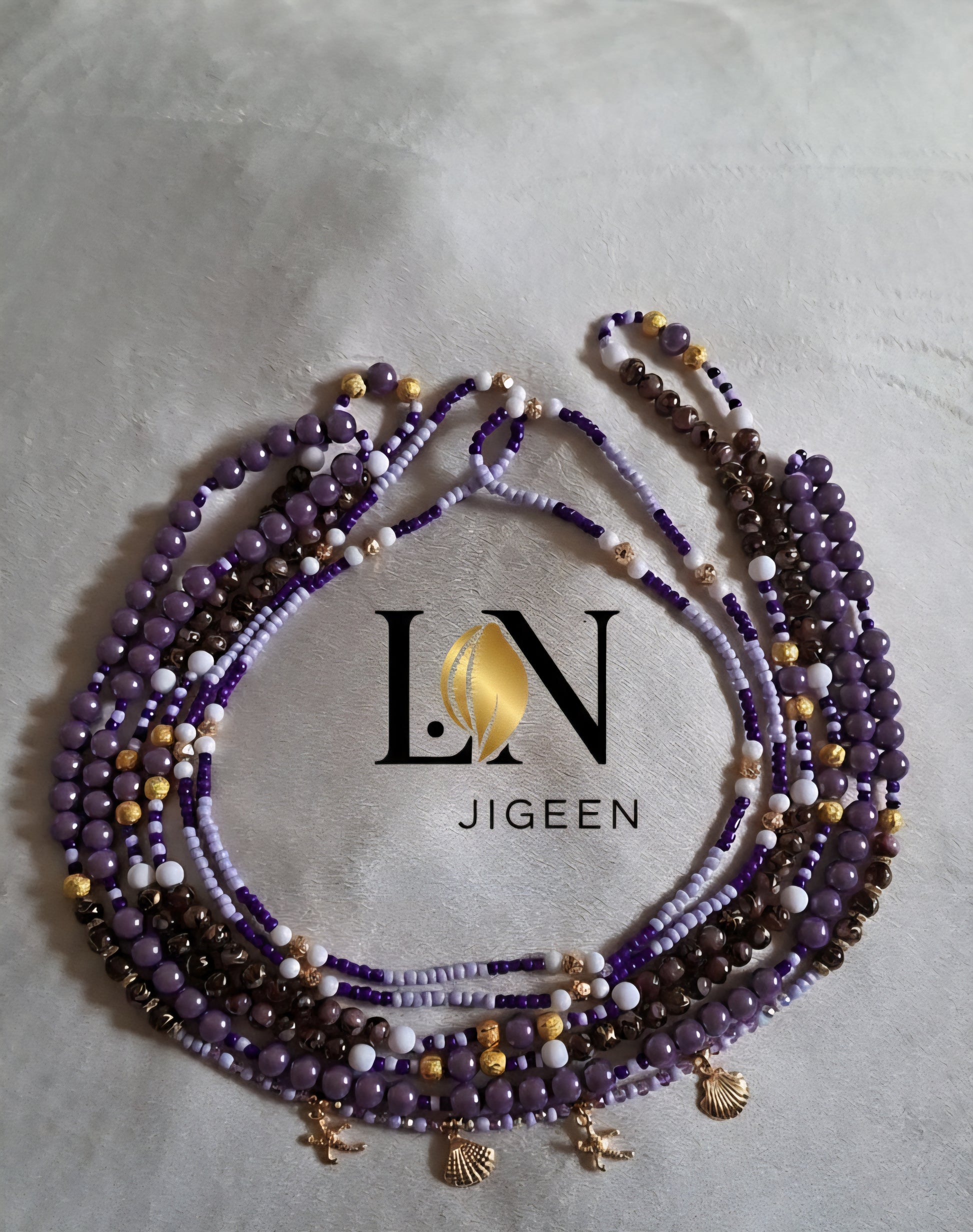 Perles de reins L.N JIGEEN violettes et dorées avec coquillages, présentées à plat sur fond clair et doux, logo central