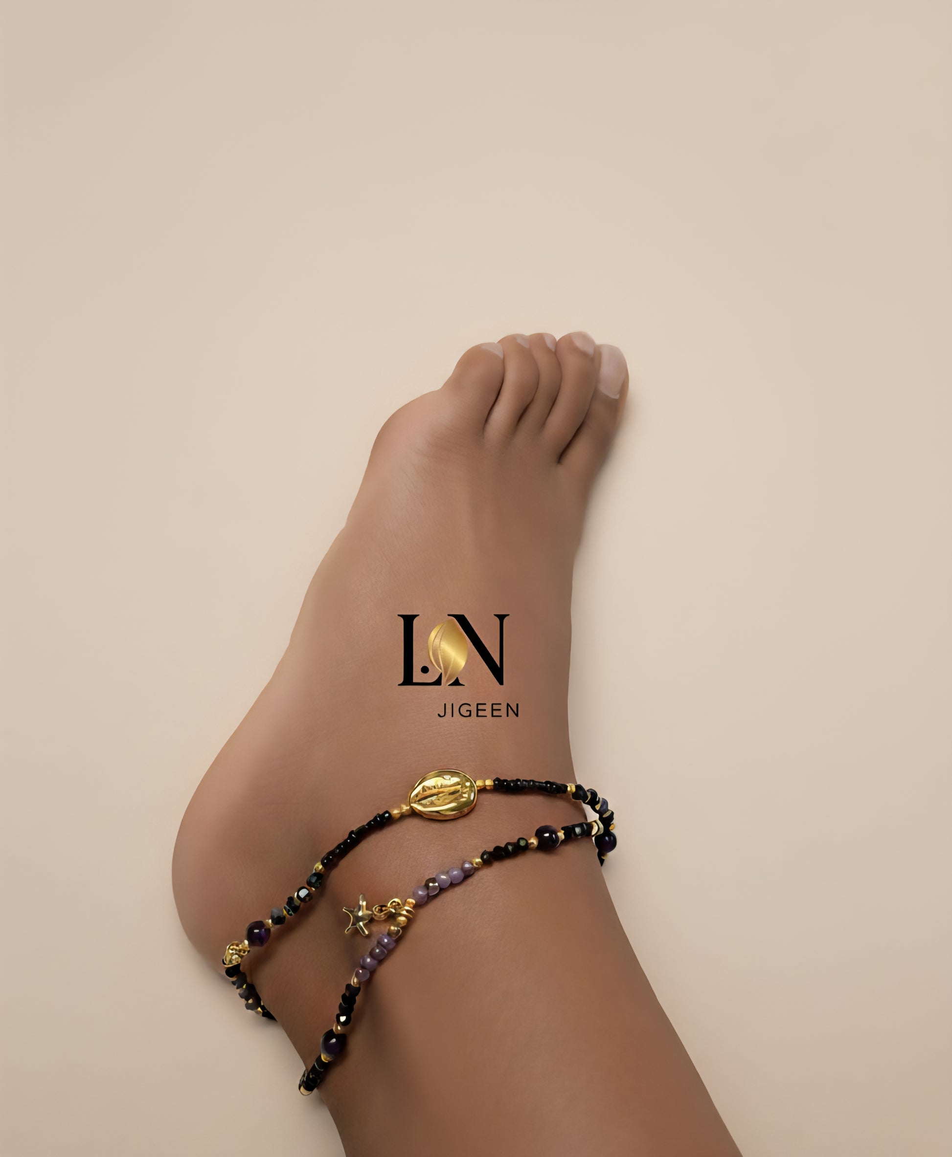 Cheville avec bracelet de cheville L.N Jigeen en perles dorées et noires, fond uni beige, logo L.N Jigeen sur le pied.