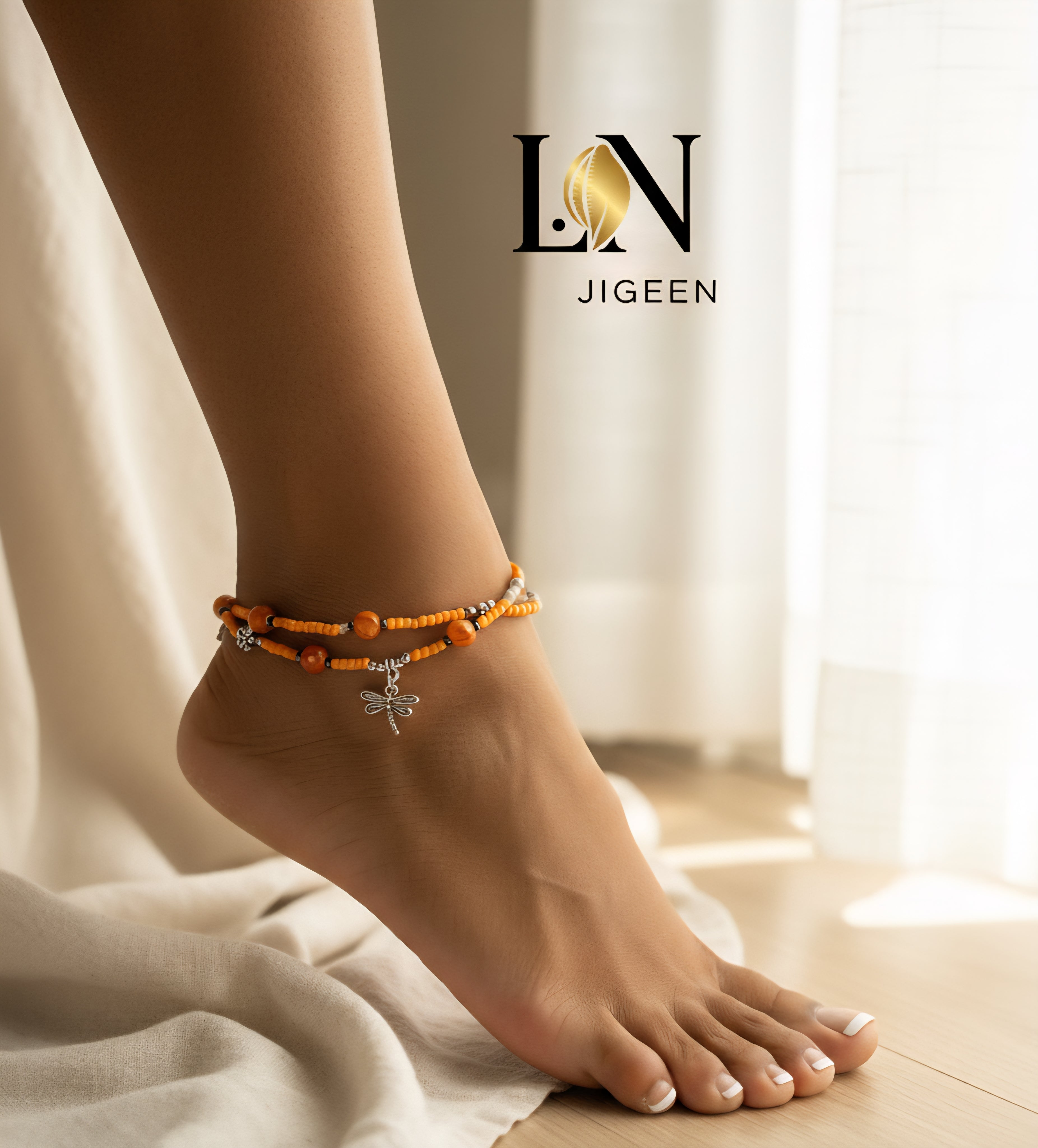 Cheville féminine manucurée portant un bracelet de cheville double rang LN JIGEEN avec perles orange et breloques libellule sur fond intime chic.