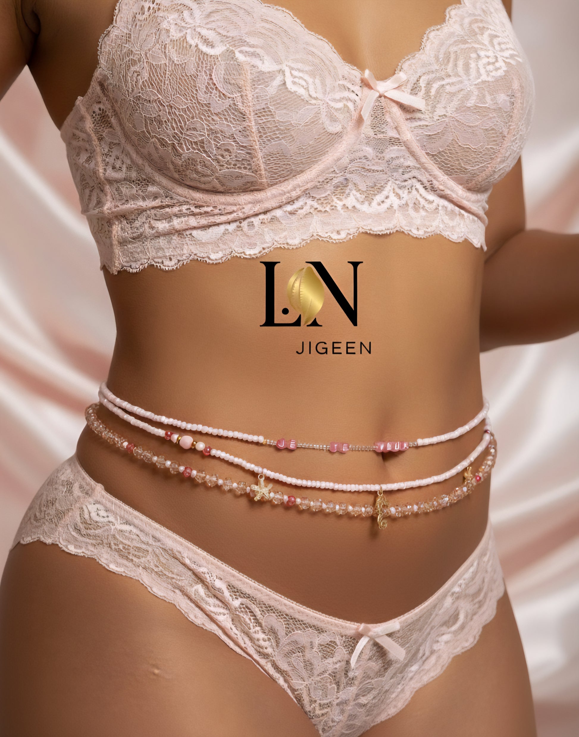 Perles de reins roses L.N JIGEEN portées par une femme noire en lingerie rose, avec le logo L.N JIGEEN centré au-dessus des bijoux, sur fond drapé rose. Les perles incluent l'inscription "JE TE VEUX" et des pendentifs étoile de mer/hippocampe.
